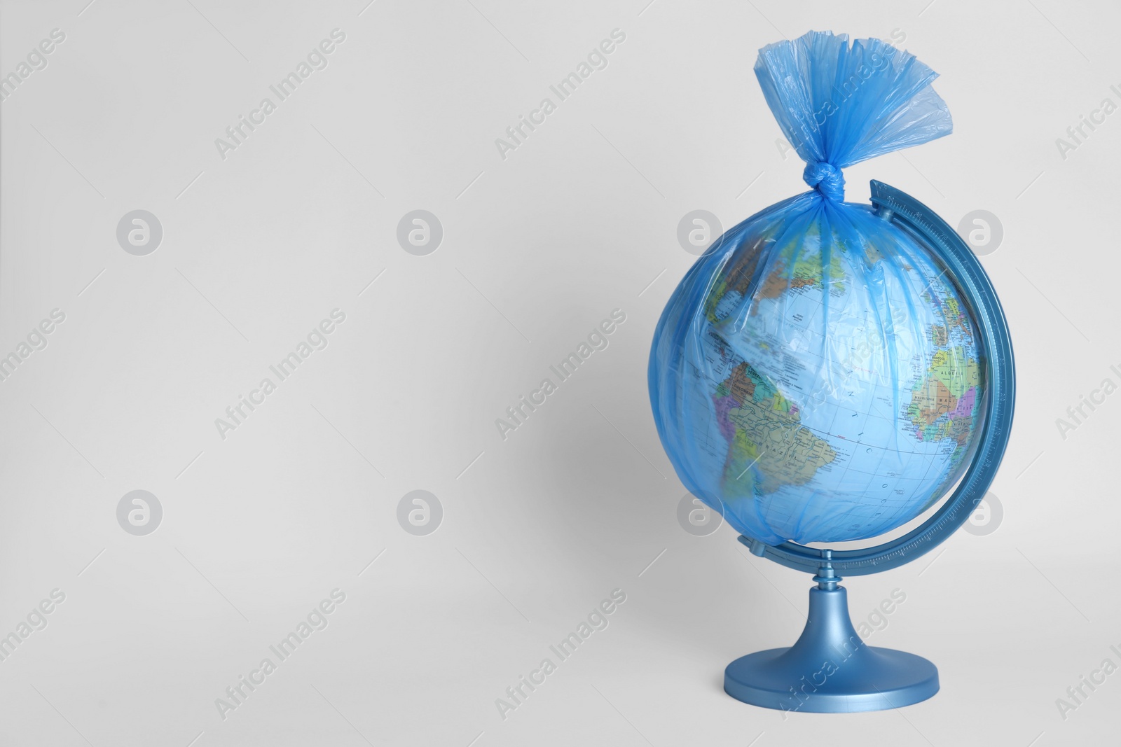 Photo of Globe in plastic bag on white background, space for text. Environmental conservation