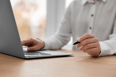 Photo of Woman with pen working on laptop at wooden table, closeup. Electronic document management