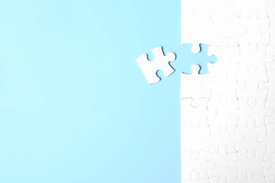 Photo of Blank white puzzle with separated piece on light blue background, flat lay. Space for text