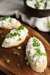 Photo of Bread with cottage cheese and green onion on wooden board, closeup