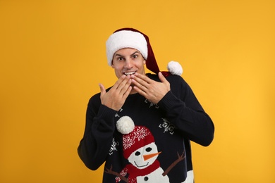 Photo of Surprised man in Christmas sweater and Santa hat on yellow background
