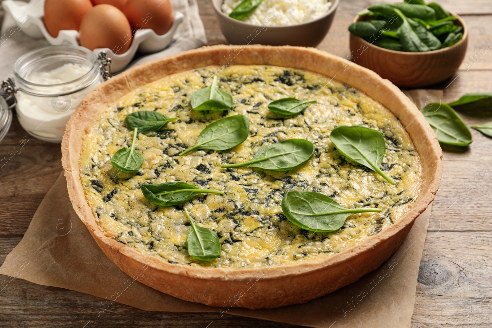 Photo of Delicious homemade spinach pie and fresh ingredients on wooden table, closeup