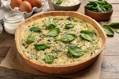 Photo of Delicious homemade spinach pie and fresh ingredients on wooden table, closeup