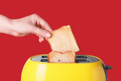 Woman taking roasted bread out of toaster on red background, closeup