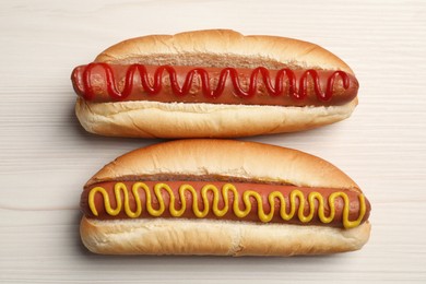 Photo of Fresh delicious hot dogs with sauces on white wooden table, top view
