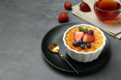 Photo of Delicious creme brulee with berries and mint in bowl on grey table. Space for text