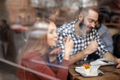 Lovely young couple spending time together in cafe, view from outdoors through window