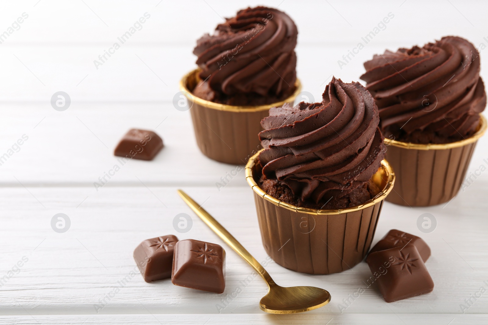 Photo of Delicious cupcakes and chocolate pieces on white wooden table. Space for text