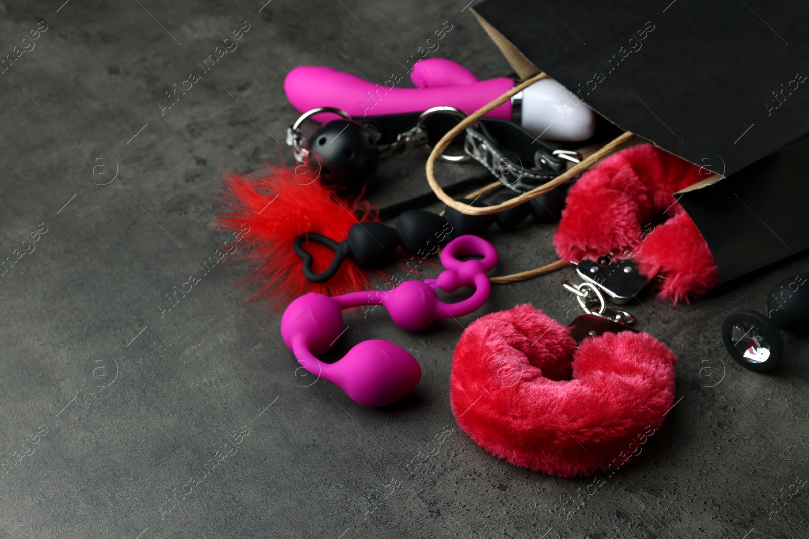 Photo of Paper shopping bag with different sex toys on grey table. Space for text