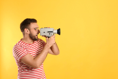 Young man using vintage video camera on yellow background, space for text