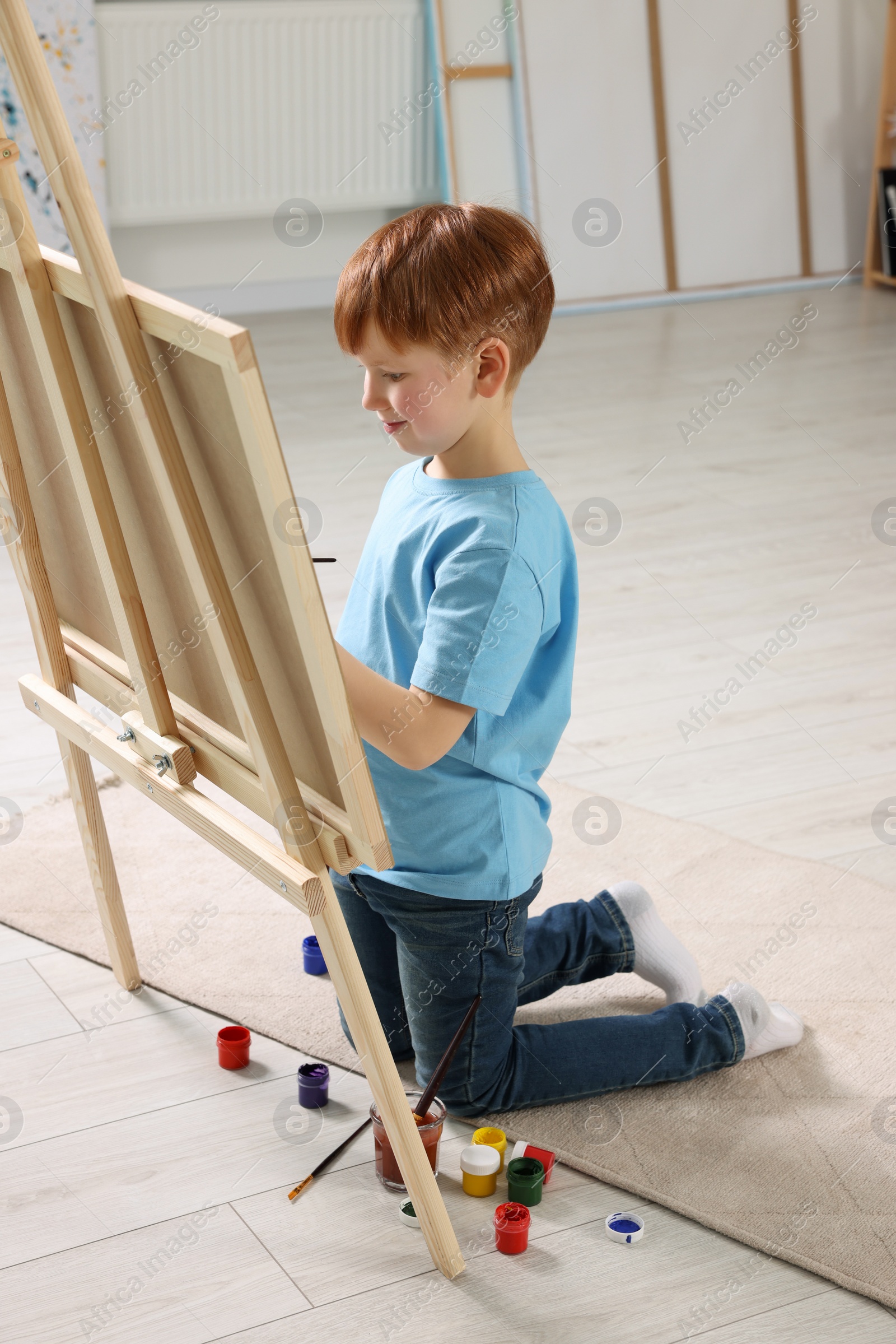 Photo of Little boy painting in studio. Using easel to hold canvas