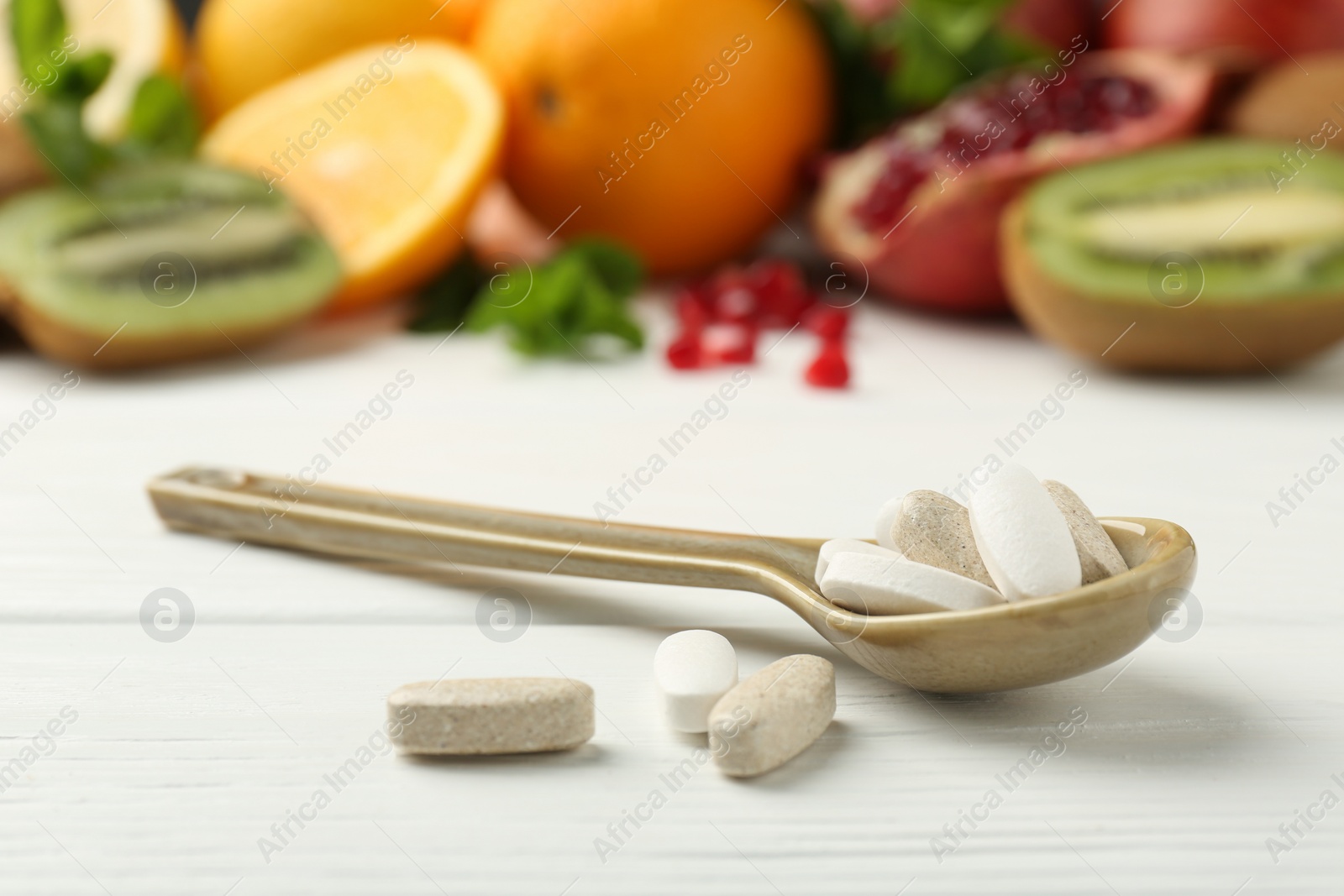 Photo of Different vitamin pills in spoon and fresh fruits on white wooden table