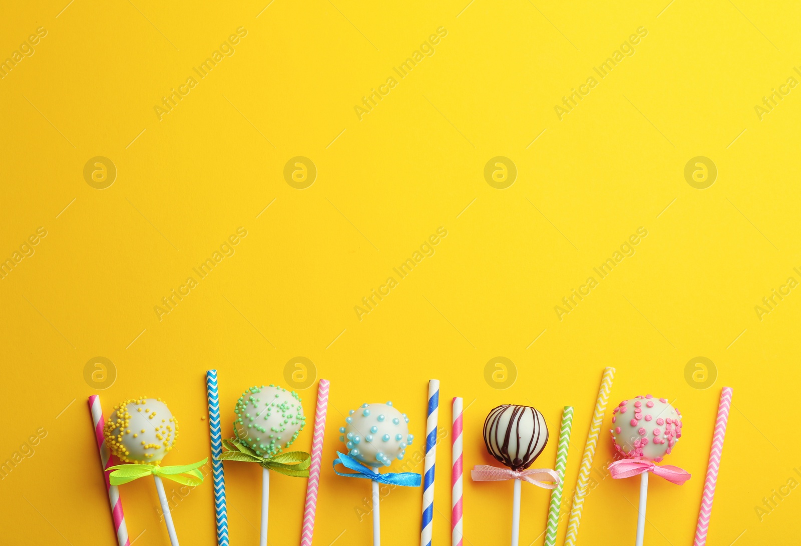 Photo of Tasty cake pops and straws on yellow background, flat lay. Space for text