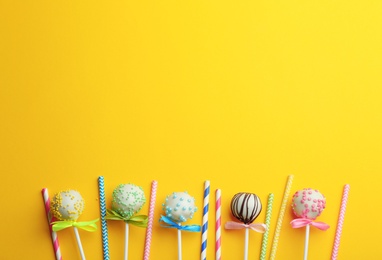 Tasty cake pops and straws on yellow background, flat lay. Space for text