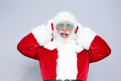 Santa Claus listening to Christmas music on color background