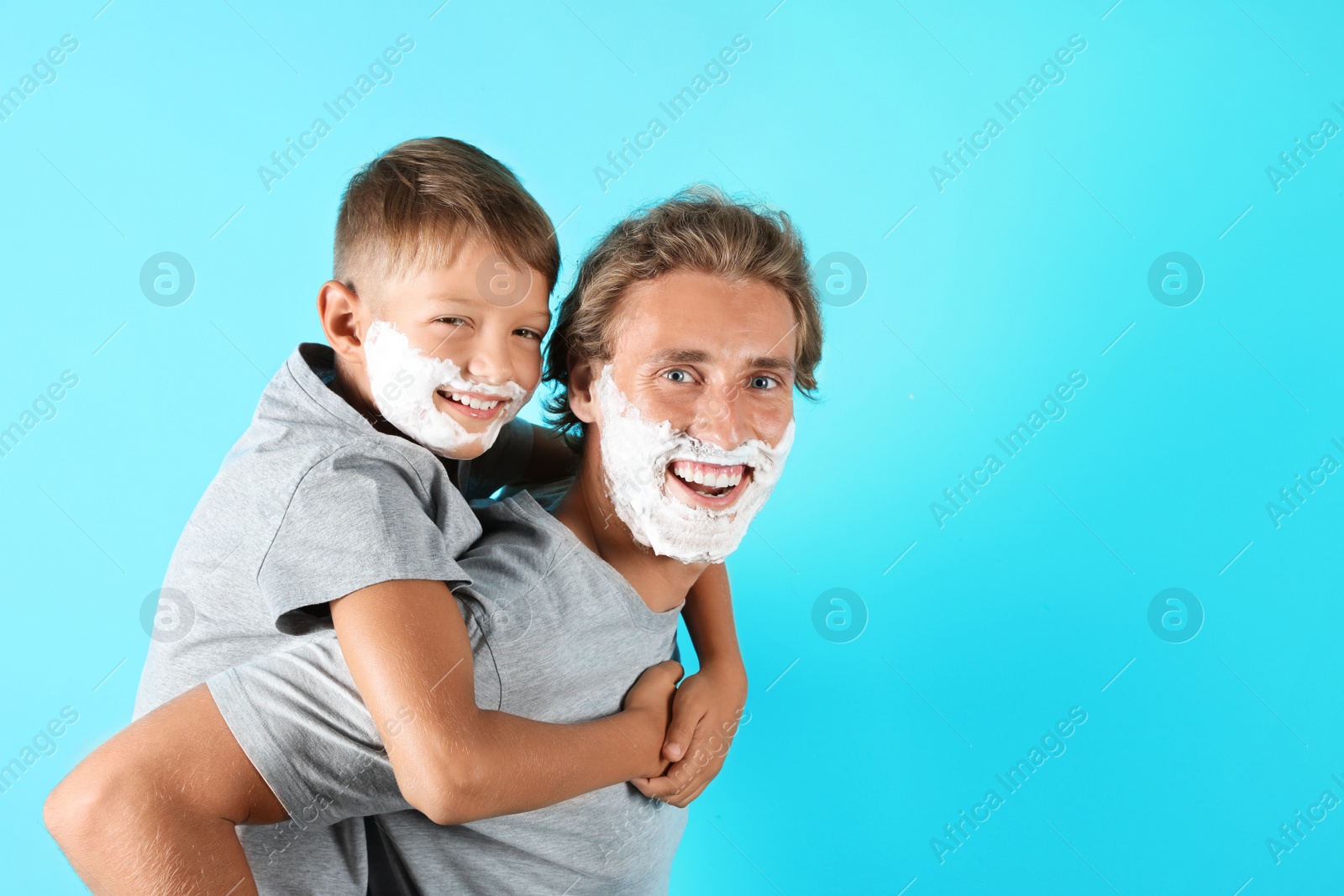 Photo of Father and son playing with shaving foam on faces against color background, space for text