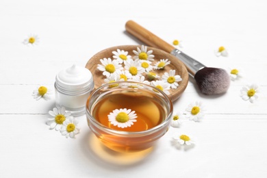 Composition with chamomile flowers and cosmetic products on white wooden table