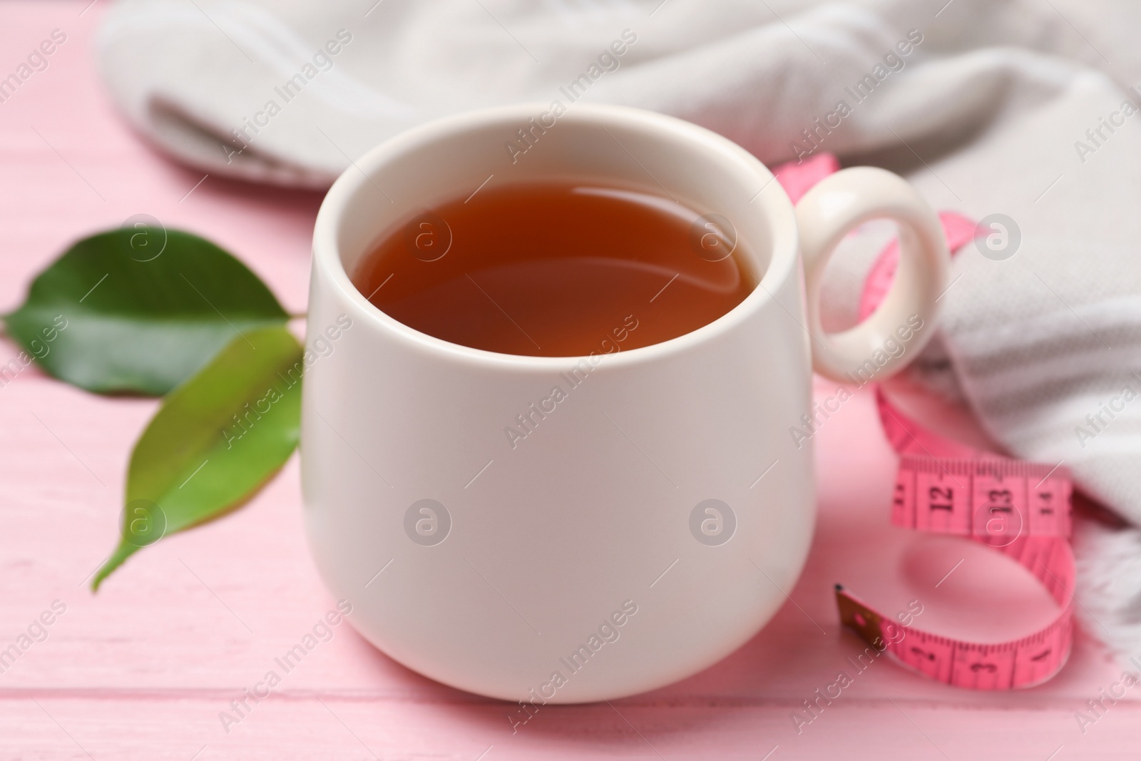 Photo of Cup of herbal diet tea and measuring tape on pink wooden table, closeup. Weight loss concept