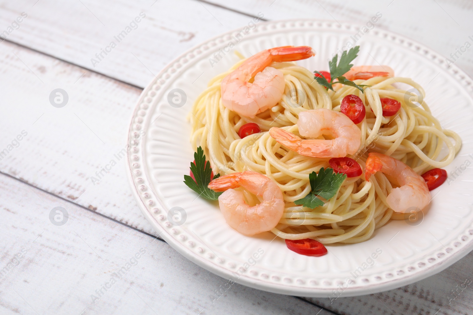 Photo of Tasty spaghetti with shrimps, chili pepper and parsley on wooden rustic table, closeup. Space for text