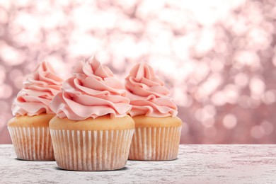 Delicious birthday cupcakes on white table against blurred lights. Space for text