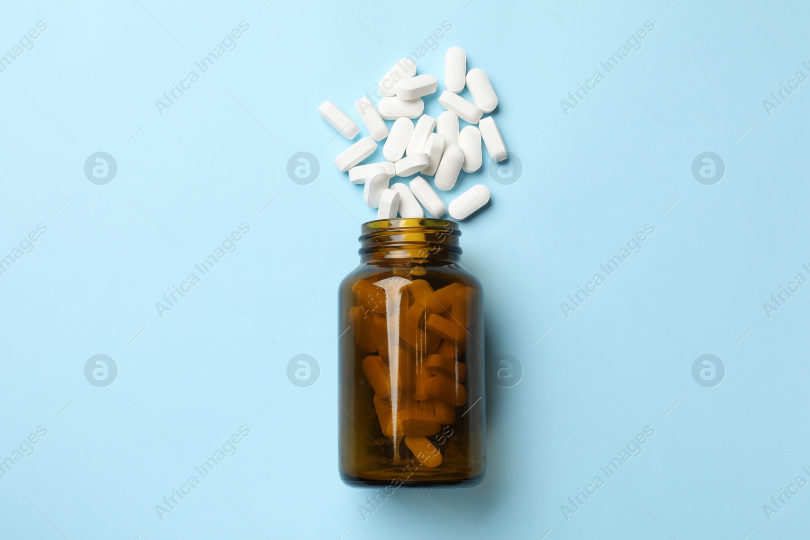 Photo of Vitamin pills and bottle on light blue background, top view