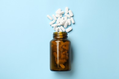 Photo of Vitamin pills and bottle on light blue background, top view