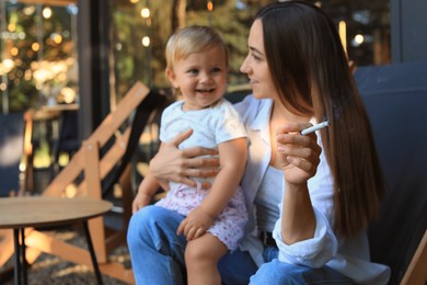 Photo of Mother with cigarette and child outdoors, focus on hand. Don't smoke near kids