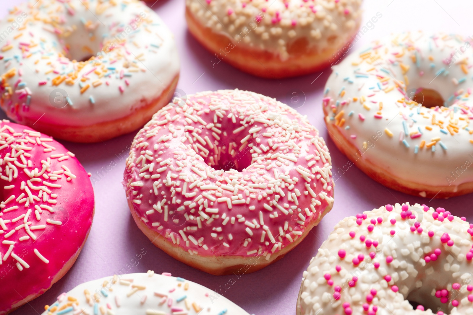 Photo of Delicious glazed doughnuts with sprinkles on color background