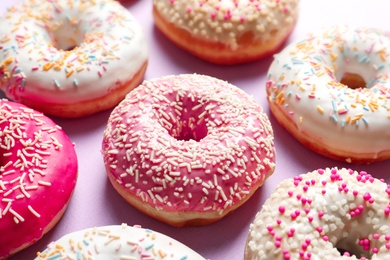 Delicious glazed doughnuts with sprinkles on color background