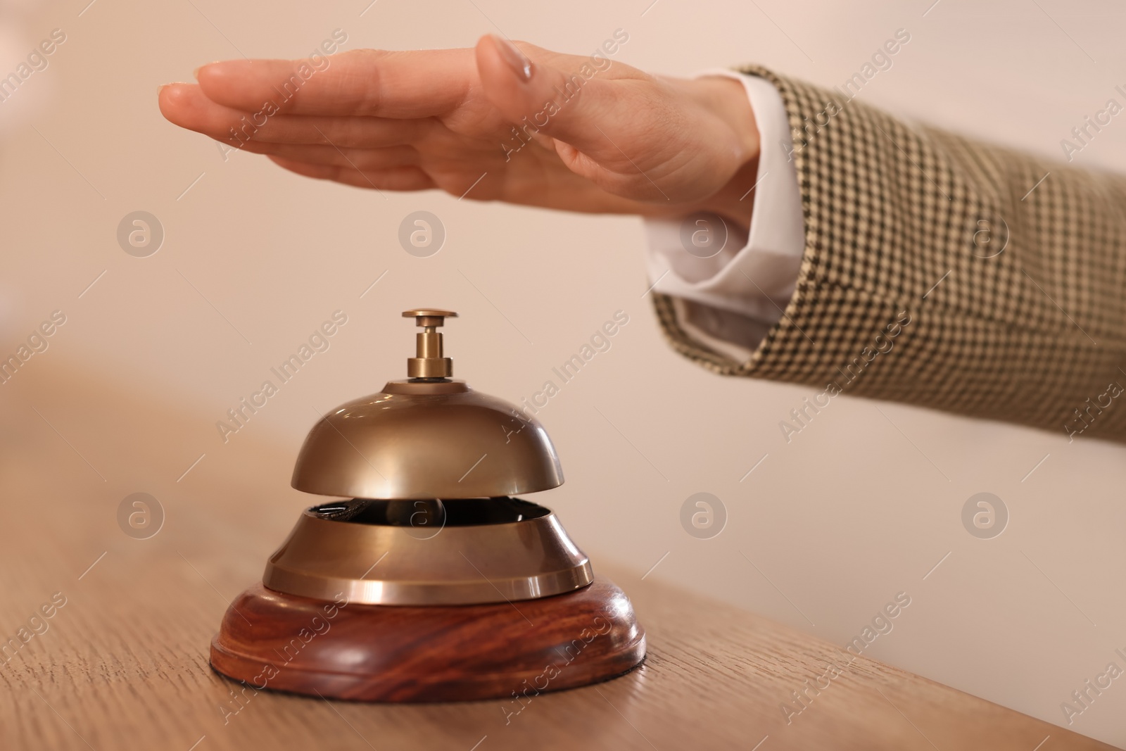 Photo of Woman ringing hotel service bell at wooden reception desk, closeup