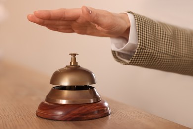 Photo of Woman ringing hotel service bell at wooden reception desk, closeup