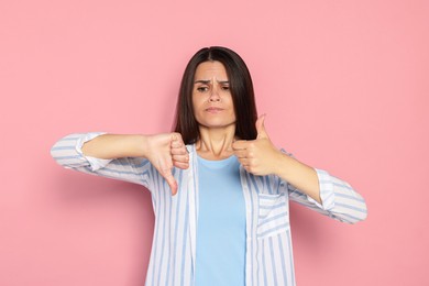 Young woman showing thumbs up and down on pink background