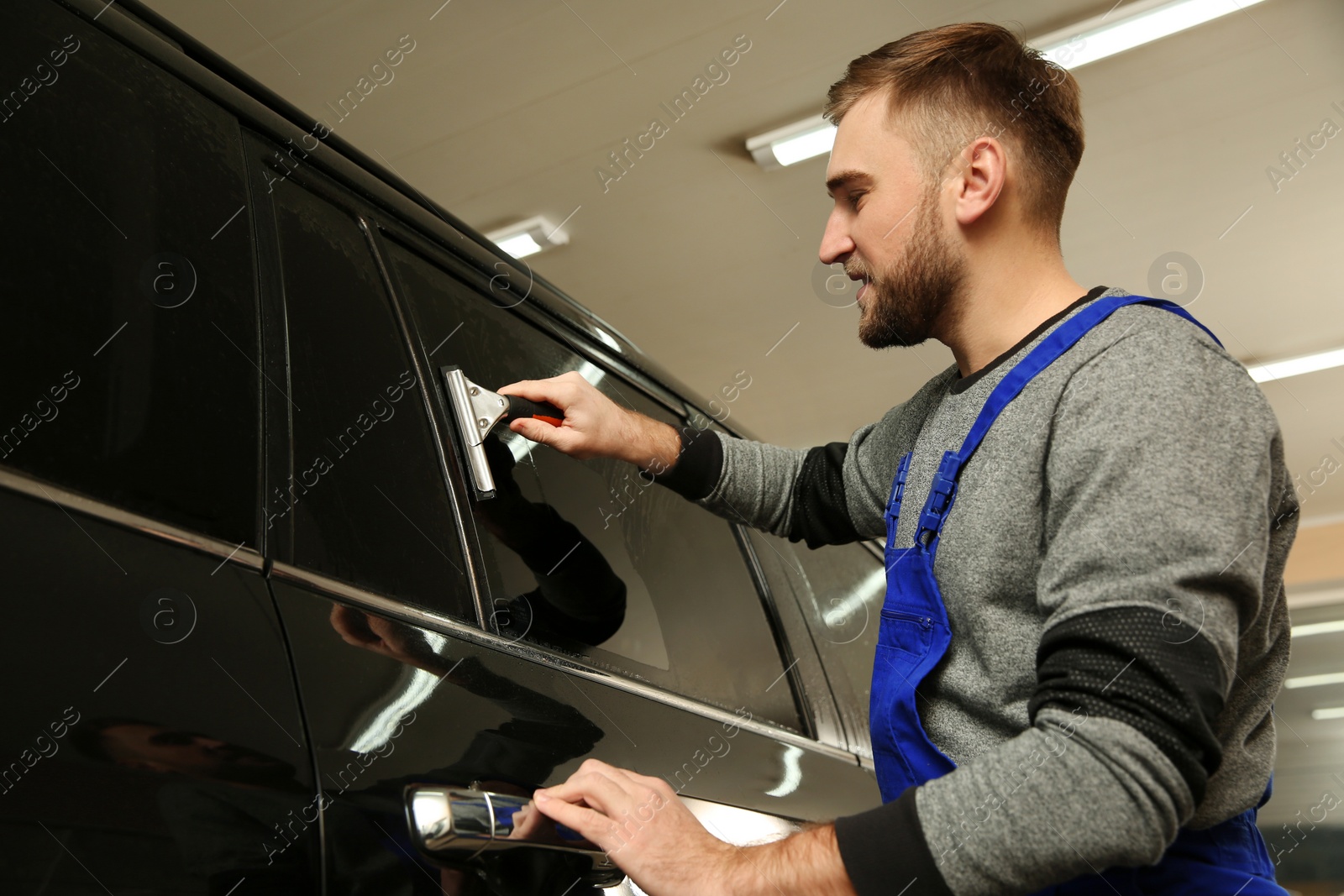 Photo of Skilled worker washing tinted car window in shop