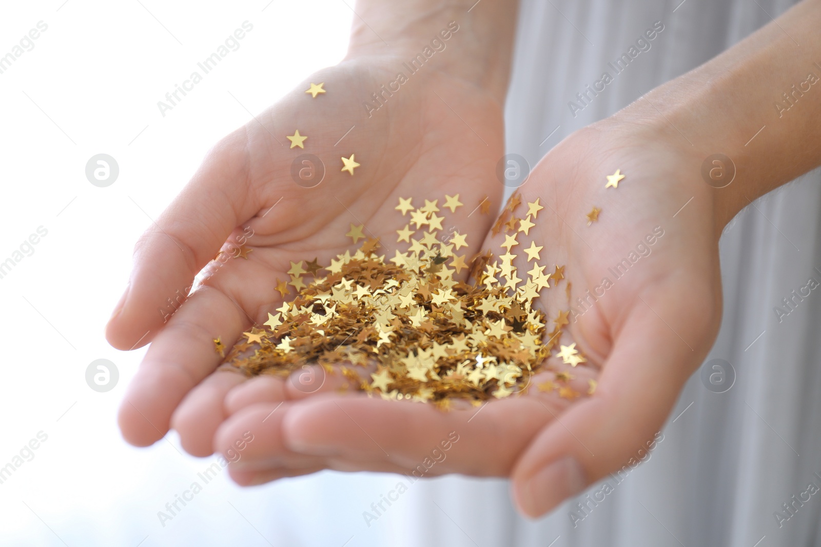 Photo of Woman holding gold confetti stars on light background, closeup. Christmas celebration