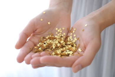Photo of Woman holding gold confetti stars on light background, closeup. Christmas celebration
