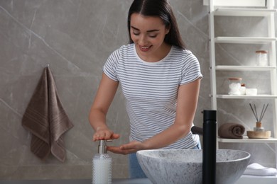 Young woman washing hands with liquid soap in bathroom