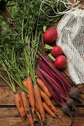 Photo of Different vegetables and net bag on wooden table, flat lay