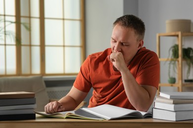 Tired man studying at wooden table indoors