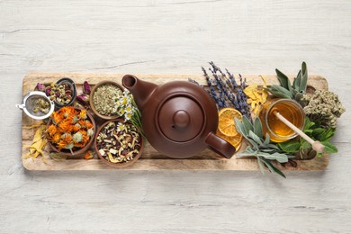 Photo of Clay teapot, honey and different dried herbs on white wooden table, top view