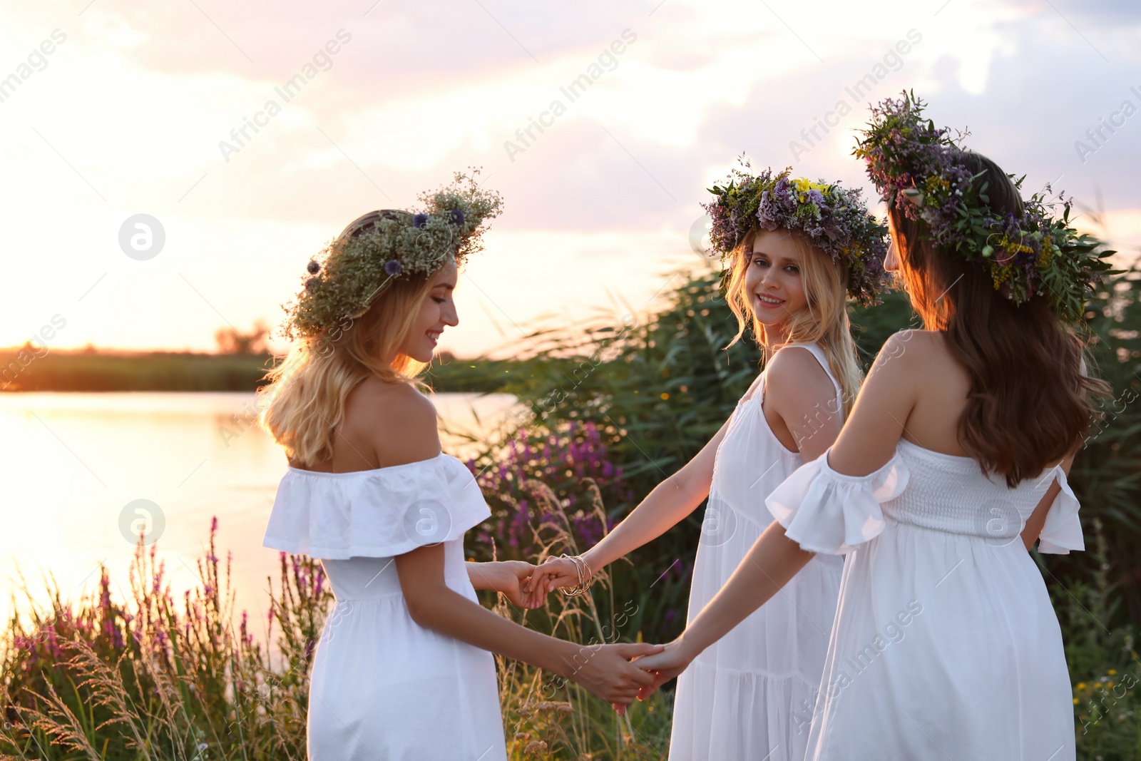 Photo of Young women wearing wreaths made of beautiful flowers outdoors at sunset