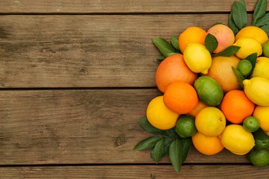 Different citrus fruits with green leaves on wooden table, flat lay. Space for text