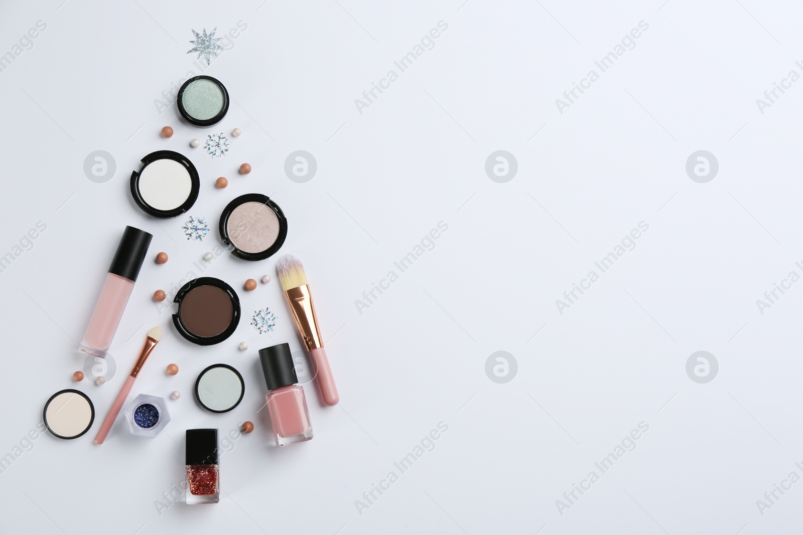 Photo of Christmas tree shape of decorative cosmetic products on light background, flat lay with space for text. Winter care