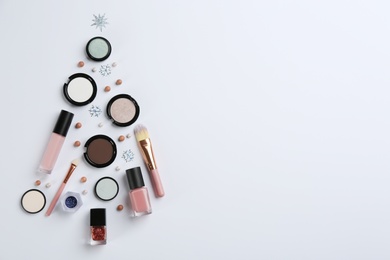 Photo of Christmas tree shape of decorative cosmetic products on light background, flat lay with space for text. Winter care