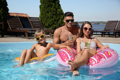 Happy family with inflatable rings and cocktails in outdoor swimming pool on sunny summer day