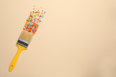 Photo of Brush painting with colorful sprinkles on beige background, top view. Space for text. Creative concept