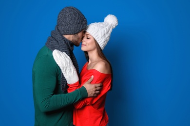 Young couple in warm clothes on color background. Christmas celebration