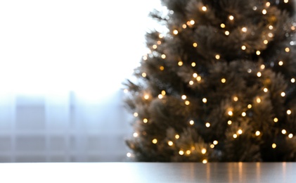 Photo of Blurred view of beautiful Christmas tree with yellow lights near window indoors, focus on table. Space for text