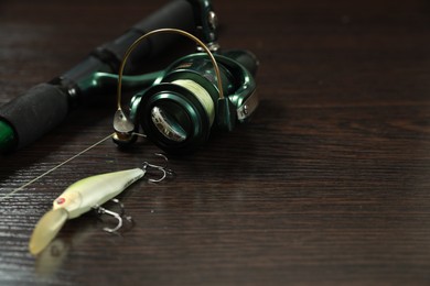 Modern fishing rod with reel and lure on dark wooden background, closeup. Space for text