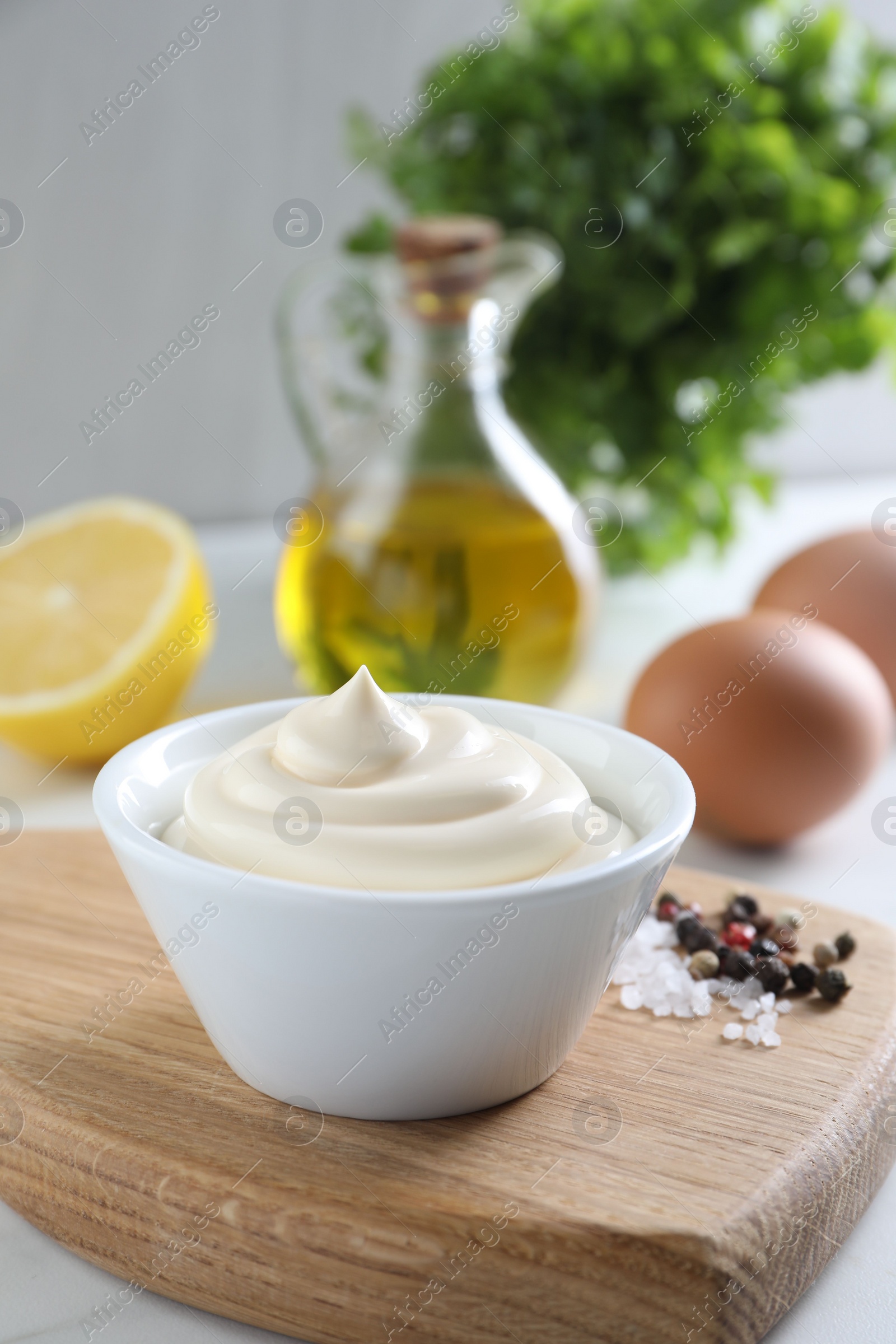 Photo of Tasty mayonnaise sauce in bowl, spices and ingredients on white table, closeup