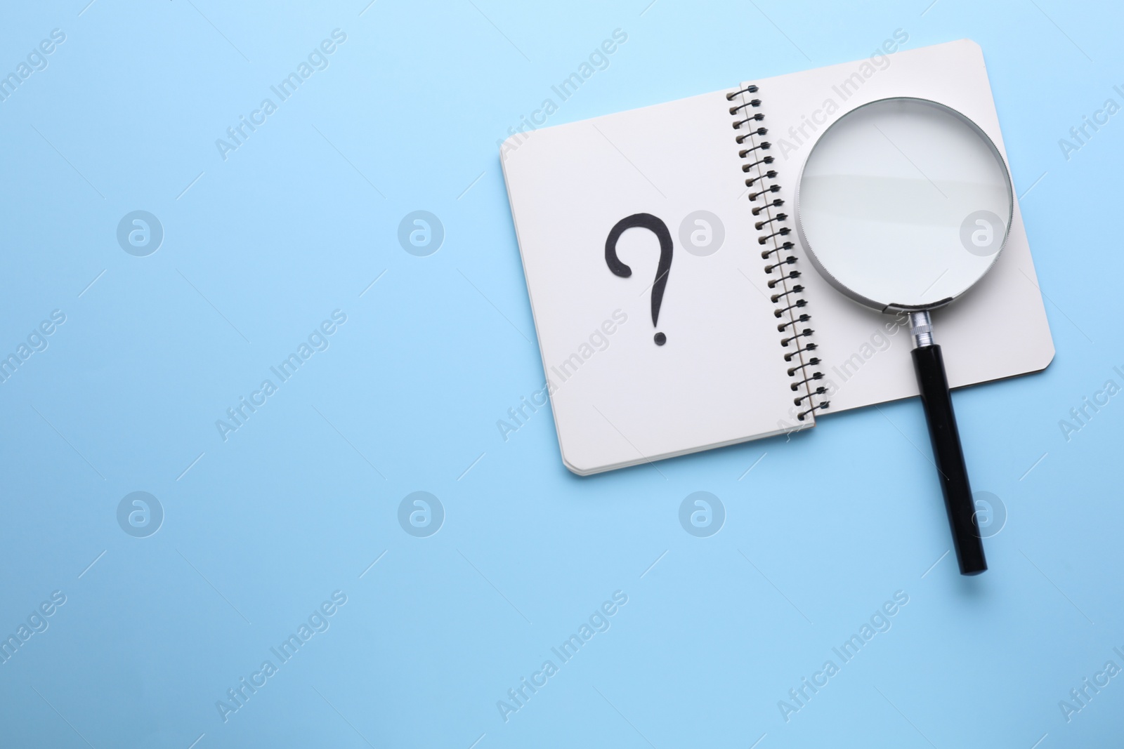 Photo of Magnifying glass and notebook with question mark on light blue background, top view. Space for text